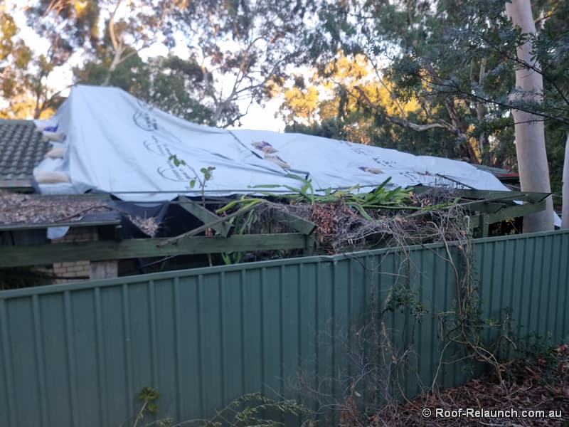 House with damaged tile roof and verandah, covered by a tarp