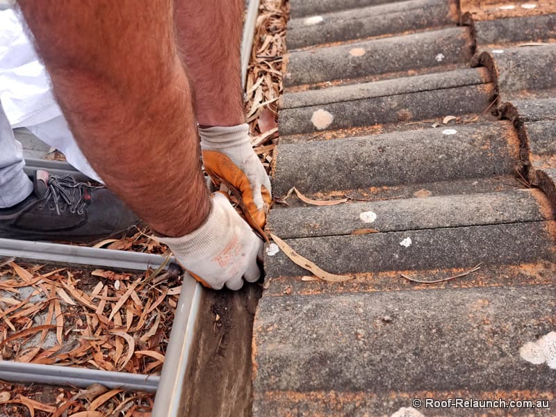 Closeup of man with gloves standing on roof, scooping out old leaves from gutter, cleaning it