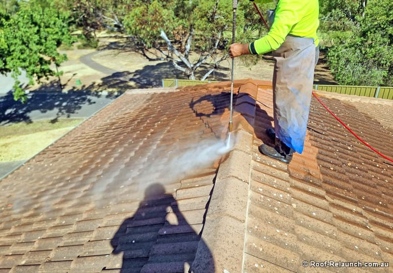 Man standing on tile roof, cleaning roof with high pressure water